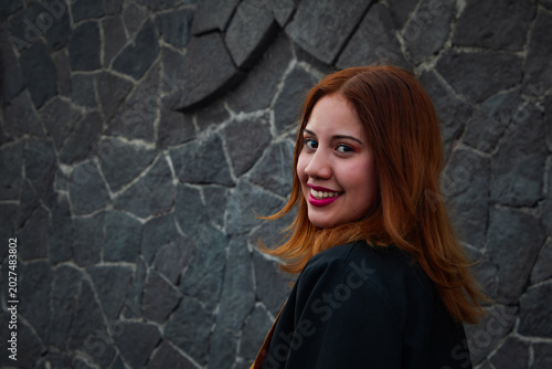 A young woman with long, reddish hair looks over her shoulder at the camera