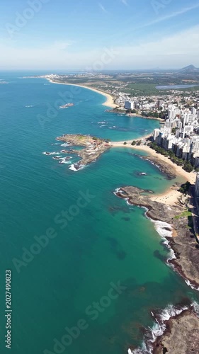 Panoramic aerial drone view of Guarapari, Espírito Santo, Brazil, with tropical beaches, turquoise Atlantic Ocean, urban coastline, rocky shores and mountains in the background.