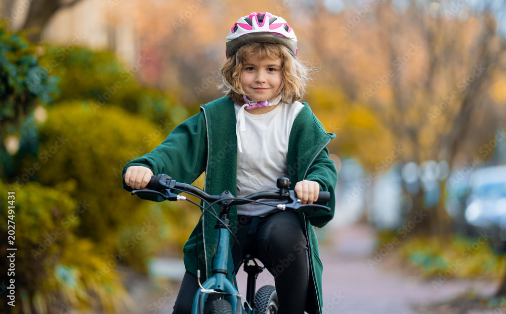 Fototapeta premium Fall city scene with child on bike. Child rides bike on autumn. Safe kid cycling on street. Happy child learning to bike ride. Child with bicycle in autumn fall park.