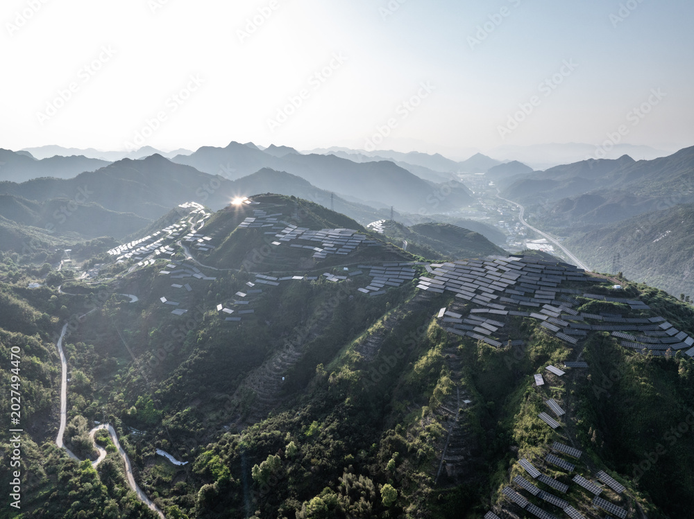 Fototapeta premium Terraced fields and village nestled in green mountains under bright sunlight
