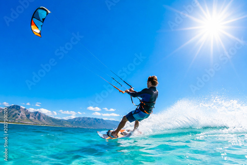 Man kitesurfing on turquoise ocean water under bright sunny sky during tropical summer vacation