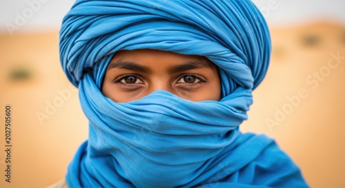 Portrait of a young Tuareg boy, blue tagelmust and traditional face veil, curious and proud gaze, Sahara Desert, North Africa