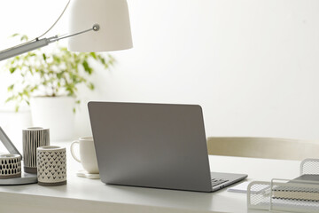 Stylish workplace with laptop, stationery, candles, cup and lamp indoors