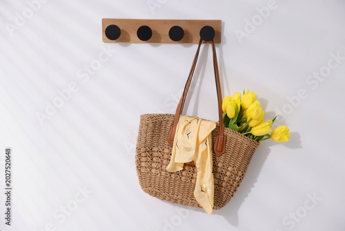 Yellow tulips in wicker bag hanging on white wall, space for text