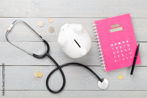 Piggy bank with stethoscope on wooden background, top view. Healthcare savings concept