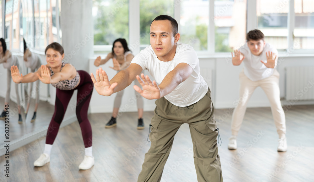 Fototapeta premium Positive sporty Asian guy doing stretching warm-up before group training in dance class for youth