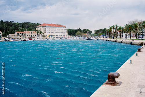 Foto Vibrant blue waves churn vigorously in a scenic port, framed by charming coastal