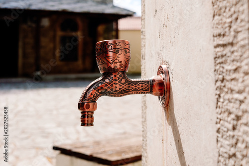 Schilderij op canvas Intricate copper faucet with Islamic patterns for ritual ablutions at a sunny mo