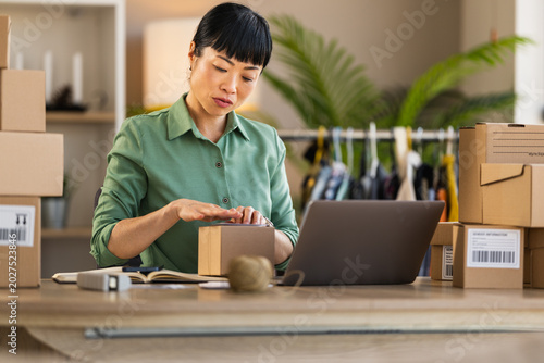 Woman packing orders for her online shop at a home office with laptop and shipping boxes