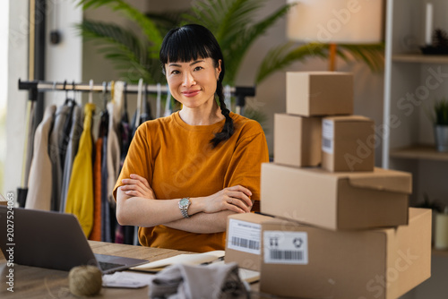 Small business owner packing orders at home office with clothing rack and laptop