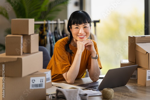 Female entrepreneur smiling at laptop surrounded by packaging boxes in home office