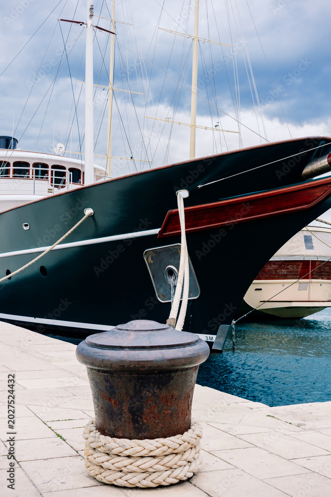 Obraz premium Textured mooring ropes loop around a sturdy bollard on the waterfront, firmly holding a sleek vessel against the calm harbor waters