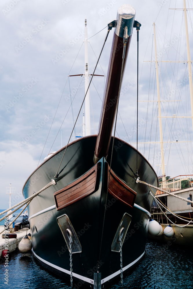 Obraz premium Dark yacht's elegant bow with wood bowsprit moored in tranquil marina, awaiting adventure