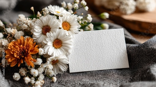Blank white card mockup with daisies and chrysanthemum flowers on grey fabric. Rustic flat lay with copy space for text
