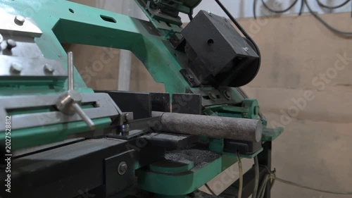 The lathe is in the production room. An electric metal cutting machine saws off a piece of metal with an automatic hacksaw to make a product
