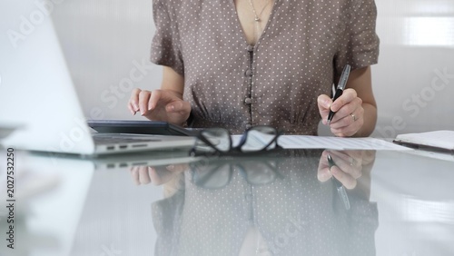 Photos Businesswoman accountant, wearing brawn dotted blouse, is using a calculator at sleek glass desk in a contemporary office