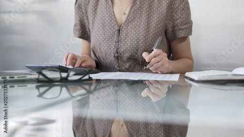 Tableau sur toile Businesswoman accountant, wearing brawn dotted blouse, is using a calculator at sleek glass desk in a contemporary office