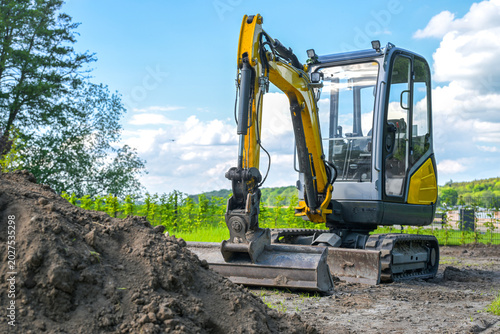 Small excavator in front of a pile of topsoil, ready to level the ground, garden and landscape architecture, blue sky, copy space, selected focus