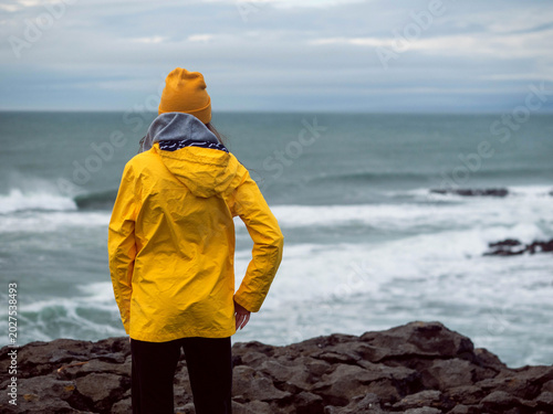 Foto Young teenager tourist in yellow jacket standing by the ocean