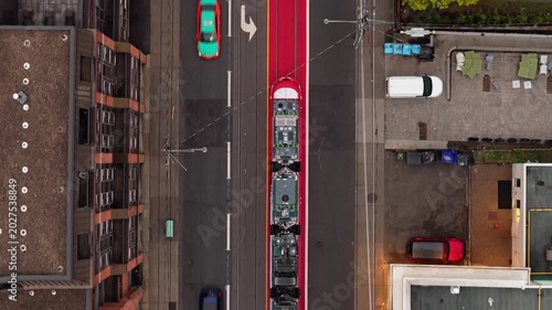 Top down aerial of a streetcar moving along a dedicated red right of way lane, cars driving beside buildings and a park in North America