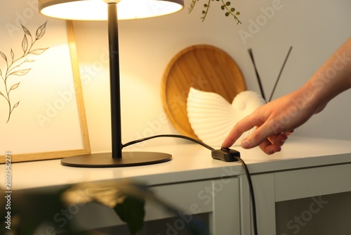Εκτύπωση καμβά Woman turning off lamp with inline cord switch on shelving unit near white wall