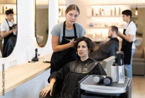 Cuadro en lienzo Young female hairdresser stylist gives haircut to adult female client in salon