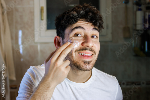 Fotografie Young man applying facial moisturizer for skincare routine and self-care wellnes