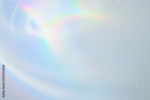 Soft pastel iridescent light leak with subtle rainbow flare on light blue background