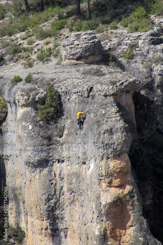 Rock climber in a yellow shirt scaling a steep limestone cliff face.
