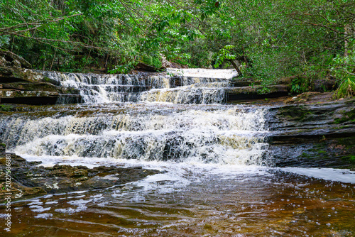 Multiple tiers of white water flow over rocky surfaces, surrounded by lush green vegetation at Las Delicias Waterfall in Colombia.