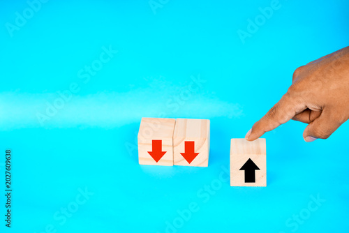 Εκτύπωση καμβά Finger selecting a wooden block with an upward arrow beside declining blocks, representing resilience, standout performance, and positive choice