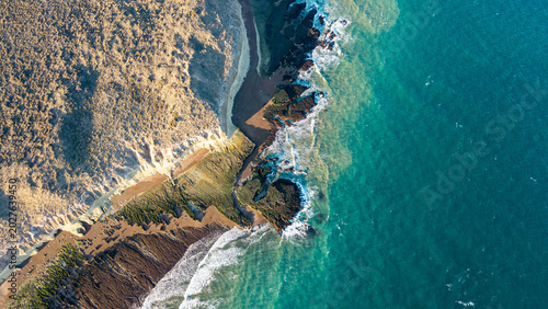 Abstract aerial view of turquoise ocean waves meeting rugged rocky coastline at golden hour.