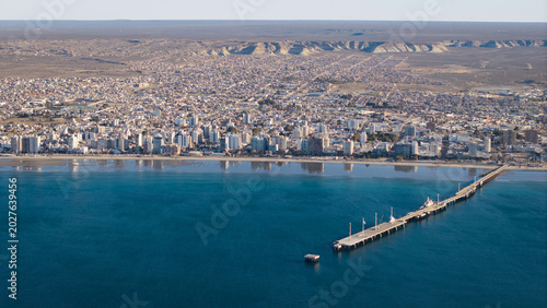 Aerial view of Puerto Madryn coastline and long pier extending into calm Atlantic Ocean waters.