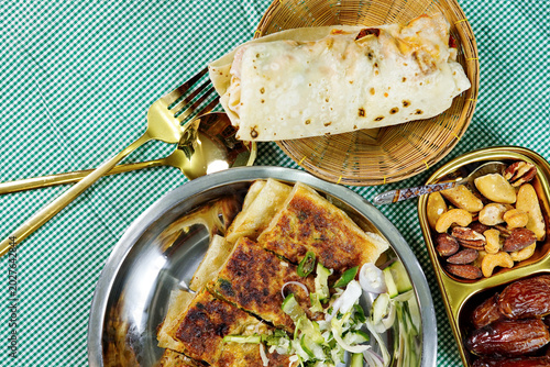 Stuffed flatbread served with crispy snacks, fresh salad and mixed nuts on festive dining table. Authentic halal street food concept for Ramadan meals and Middle Eastern cuisine themes.