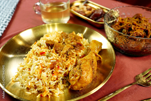 Traditional chicken biryani plate served with spicy curry, sweet dates and warm herbal tea. Authentic halal Ramadan cuisine with rich aromatic spices and elegant food presentation.