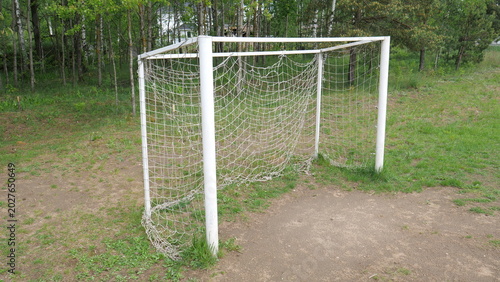 Принти на полотні Football goal with a worn net standing on a makeshift dirt pitch surrounded by g