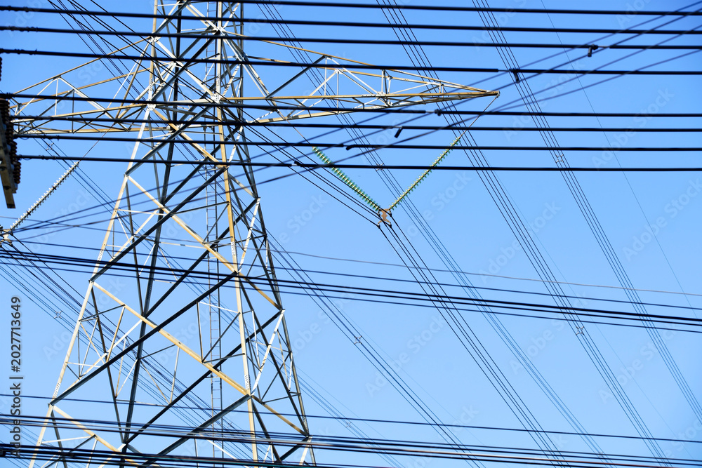 Fototapeta premium Tall High Voltage Power Transmission Tower with Multiple Power Lines Against Blue Sky