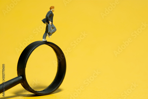 Miniature people toy figure photography. A boy pupil student running above magnifier glass. Isolated on a yellow background
