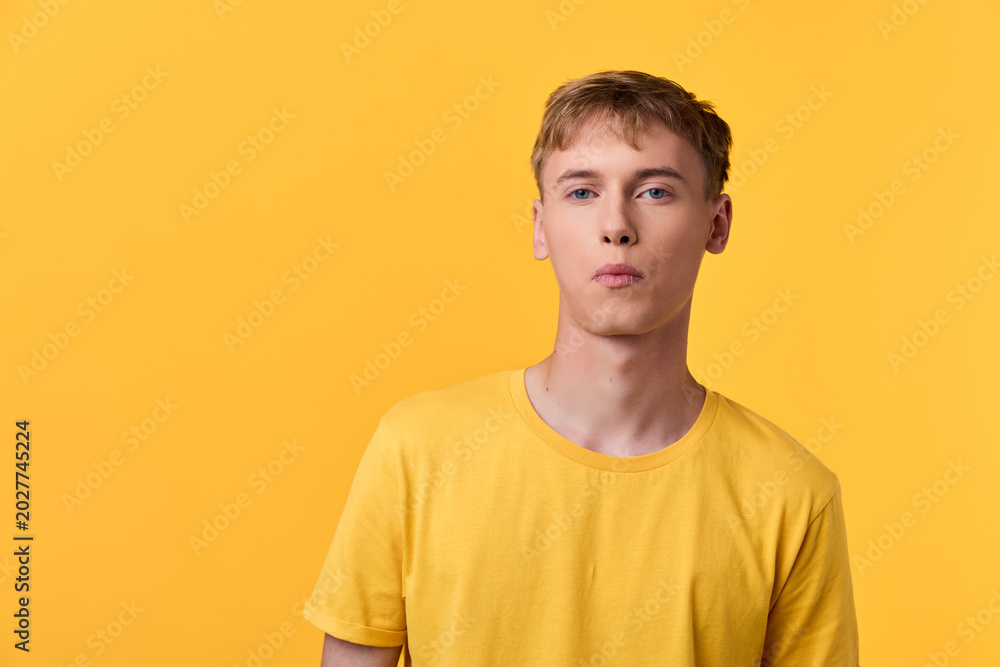 Fototapeta premium Minimalist image of a young man in a bright yellow shirt against a solid yellow backdrop, emphasizing color harmony, casual style, and contemporary fashion visual.