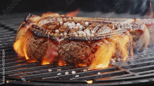 Juicy Ribeye Steak Grilling on BBQ with Flames and Coarse Salt