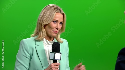 Smiling woman in mint blazer holding microphone in front of green screen