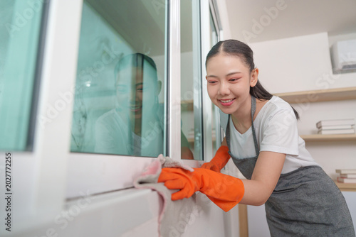 Bild auf Leinwand Asian woman in orange gloves cleaning window at modern home
