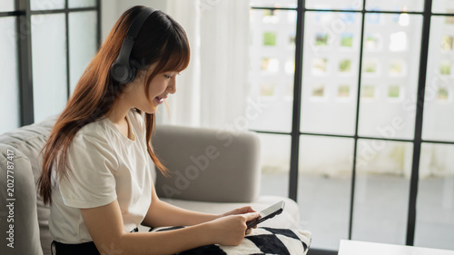 Asian woman wearing headphone listen to music and using smartphone choose playlist