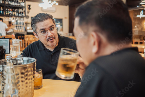 Obraz na plátne A man reacting with surprise to a friends gossip while drinking beer at the bar,