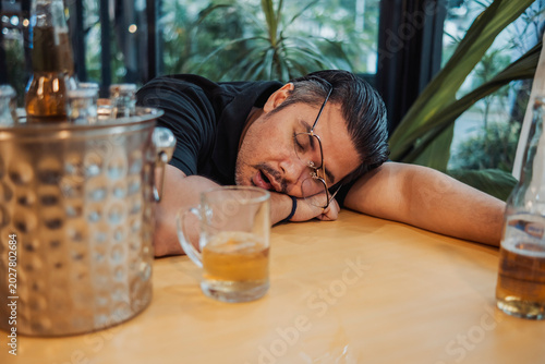 Fotografie A man passed out after heavy drinking at the bar, resting his head on the table,