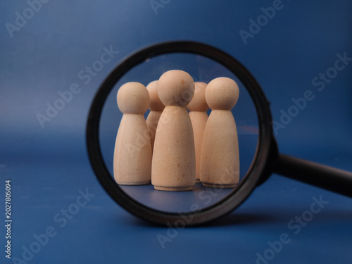 A magnifying glass focuses closely on a cluster of wooden peg dolls