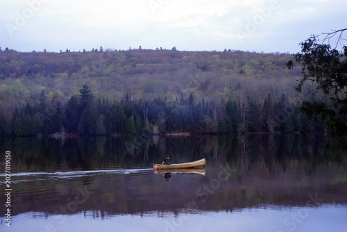Foto A lone canoeist paddles across the mirror-like surface of a calm lake at twiligh