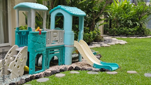 Foto Outdoor children’s playground featuring colorful slides and climbing structures surrounded by tropical garden landscaping and neatly maintained green grass