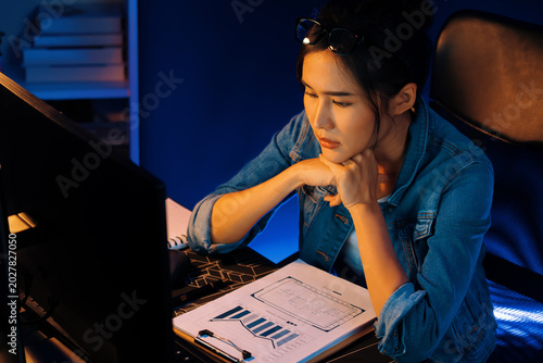 Fotografija Stressful young beautiful asian creative looking on pc to search project creator social media online with planning channel strategy reach of more viewer home at neon modern office at night