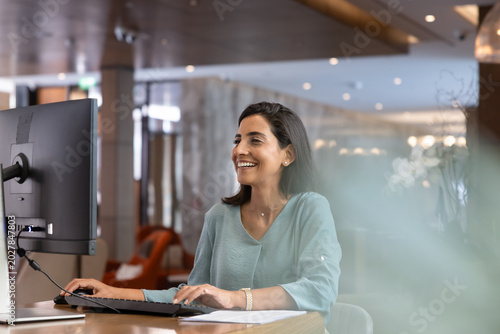 Fotografie Smiling female receptionist working on computer at reception desk, verifying res